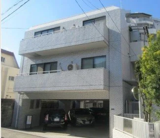 三階建ての白いマンション、駐車場に車が停まっている。