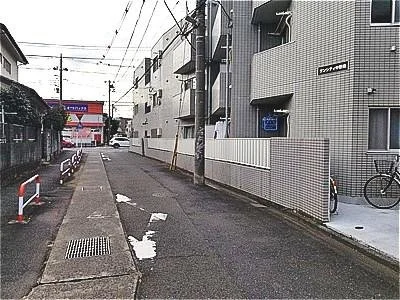 狭い街の道路と歩道、左側にフェンスと道路のホワイトライン、右側に建物と自転車