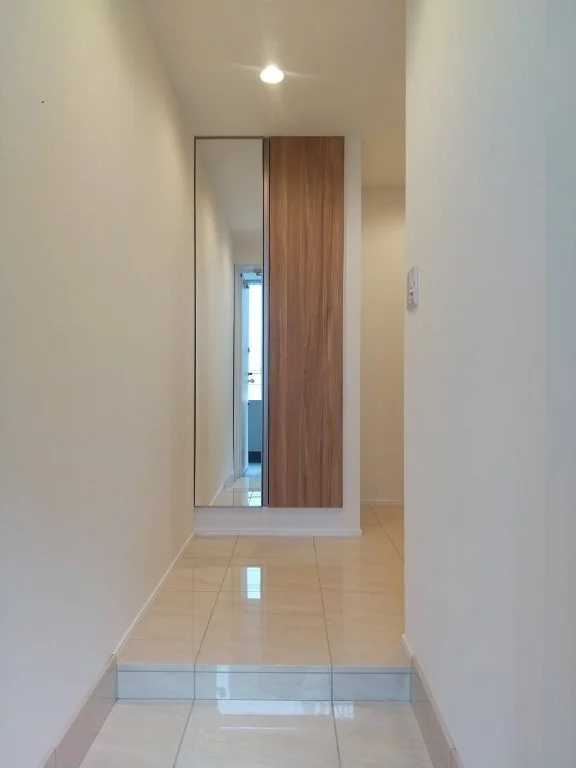 廊下の奥に木製の扉と鏡、窓が見える室内の写真