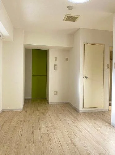 シンプルな部屋の一角。白い壁、木の床、緑色の扉が見える。