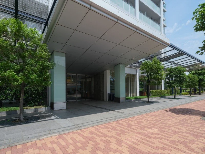 現代的なビルの入り口と周辺の歩道、公園のような緑と木々