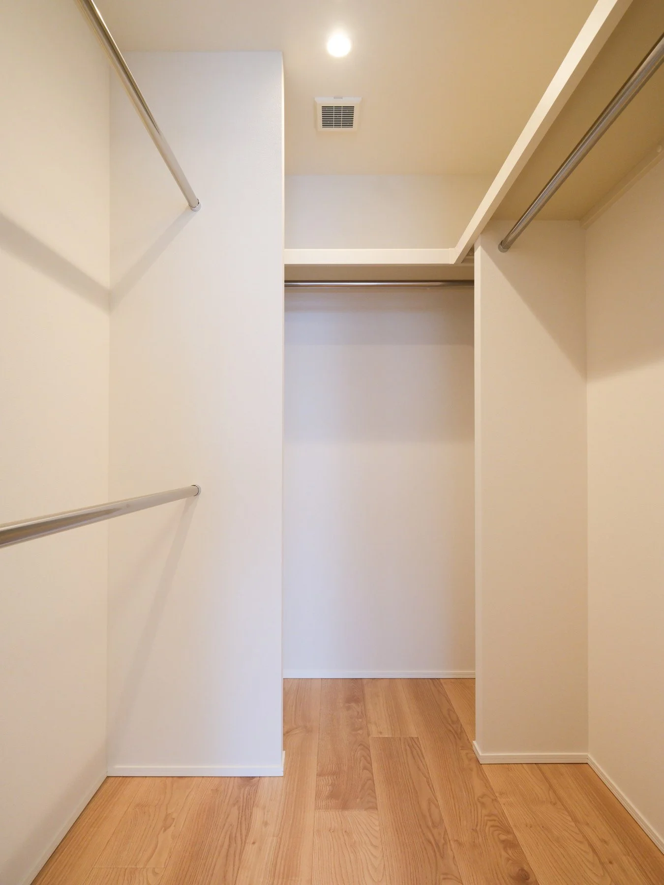 白い壁のクローゼットの内部。棚とハンガーパイプが設置されている。木製の床。