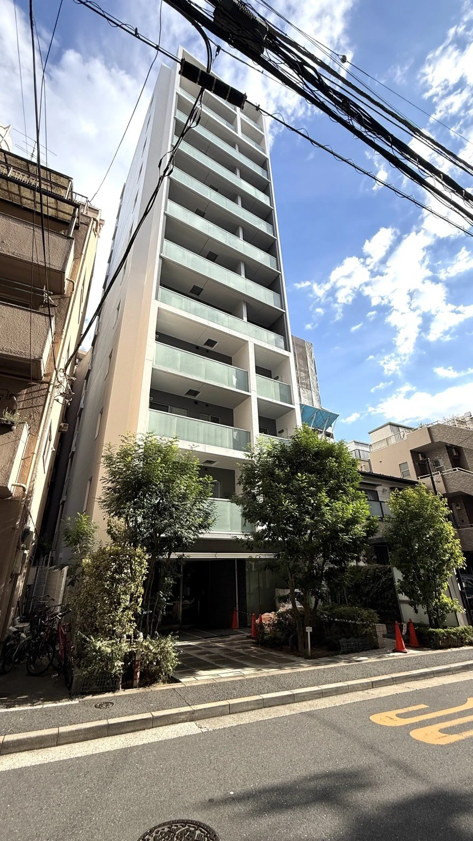 高層の白いマンションと青空、周囲には樹木とバイク。