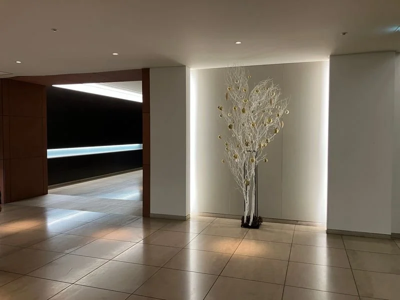 間接照明が施されたモダンな屋内ロビーに置かれた、金色の装飾が付いた白い枝のアートオブジェ