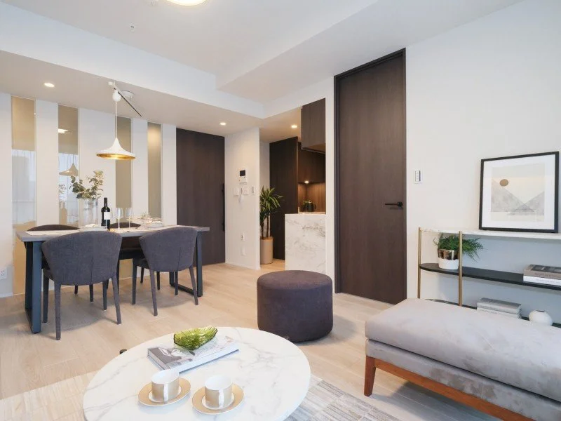 モダンなリビングルームとダイニングエリアの内観。白壁とダークウッドの家具、丸いローテーブルとコンパクトなソファがあります。