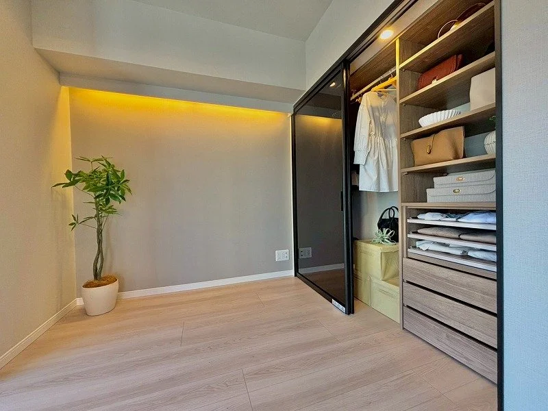 クローゼットの中に衣服とバッグが収納されている。左側に観葉植物が置かれている。