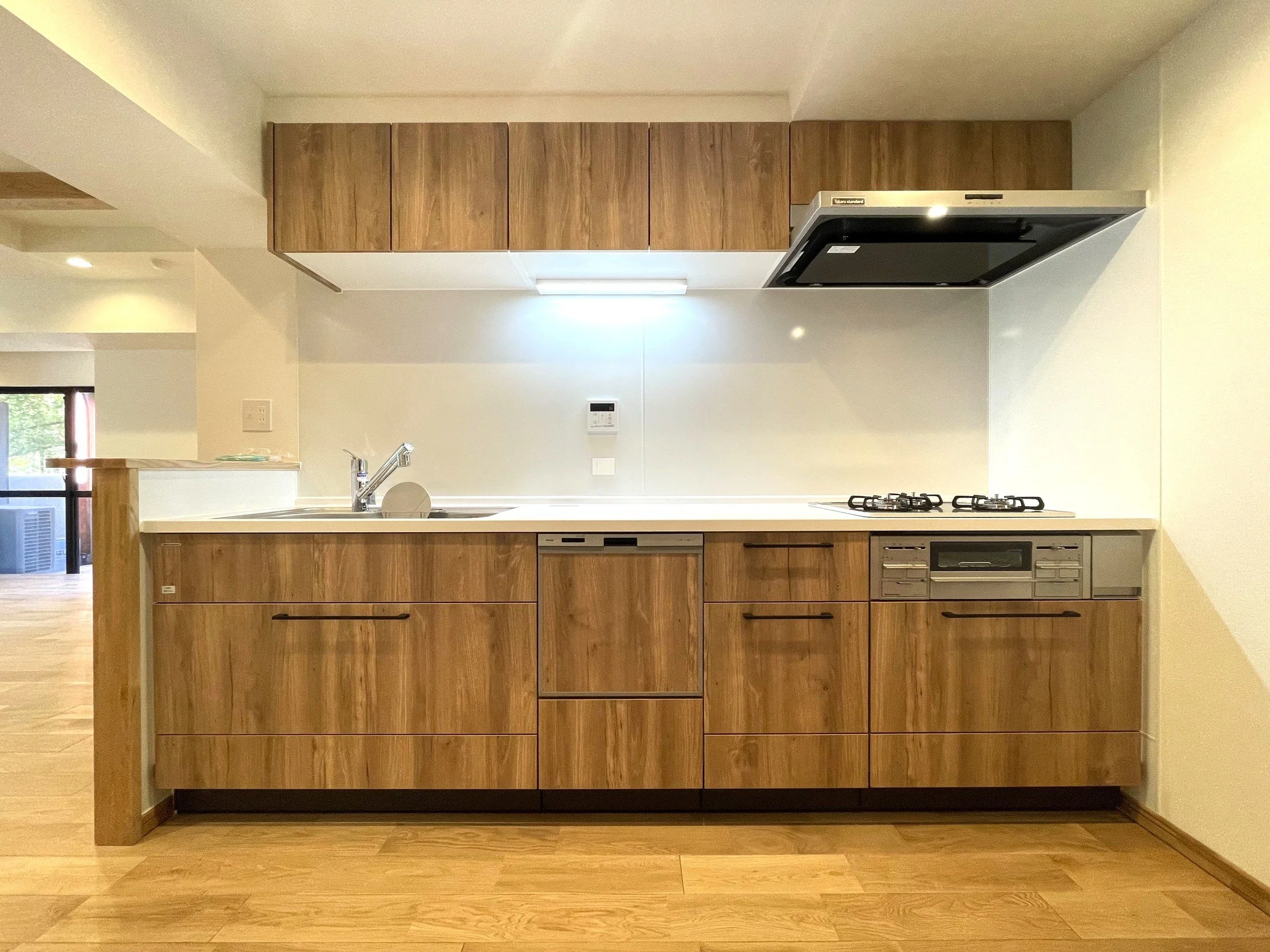 木製のキッチン収納棚とガスコンロとシンクのあるキッチンの壁面。