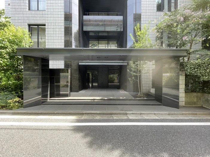 現代的な黒い建物の入り口。ガラスと石材のデザイン。周囲に緑の植物。