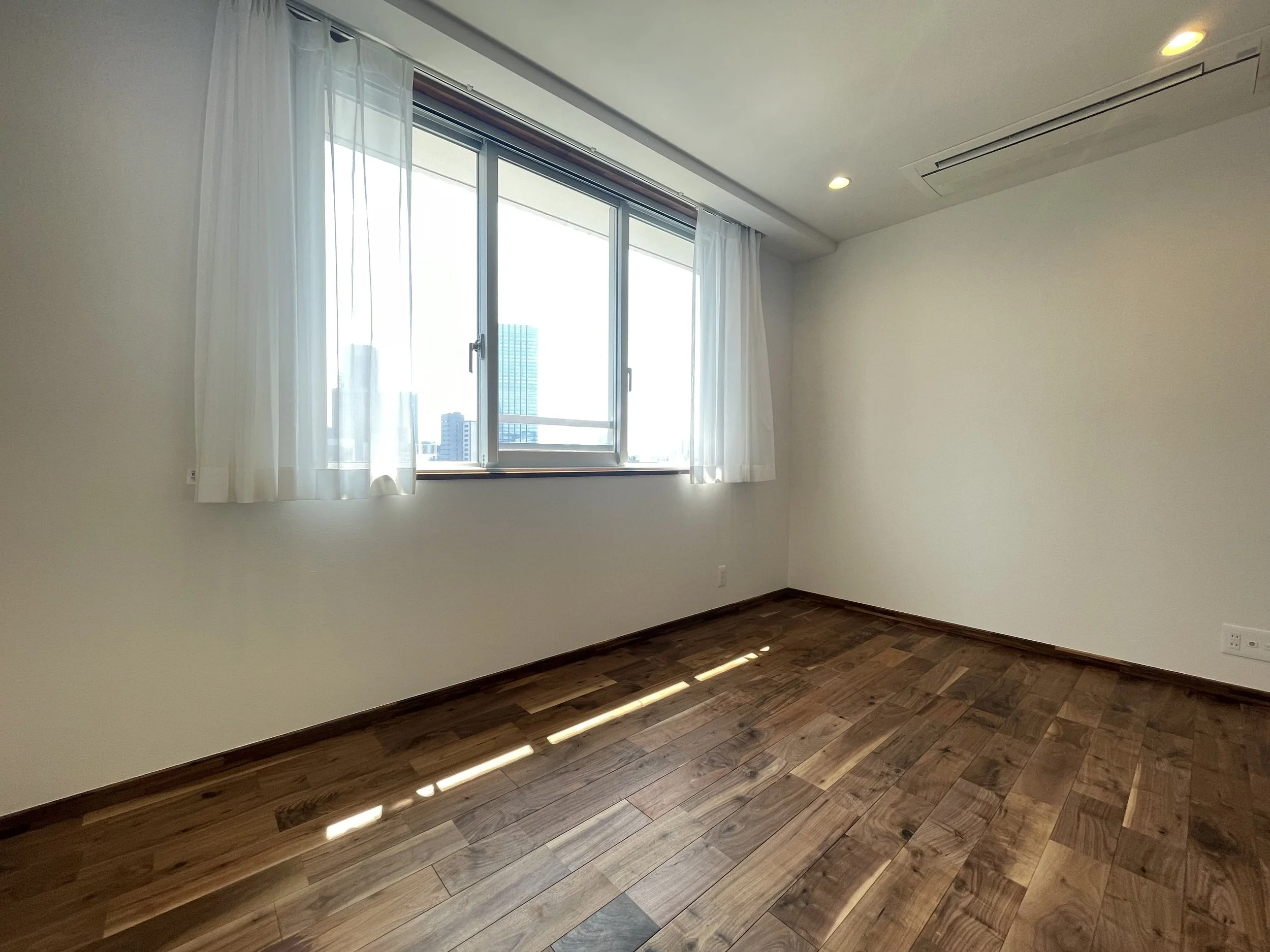 明るい空の光が差し込む、空の壁と木の床の空間の部屋