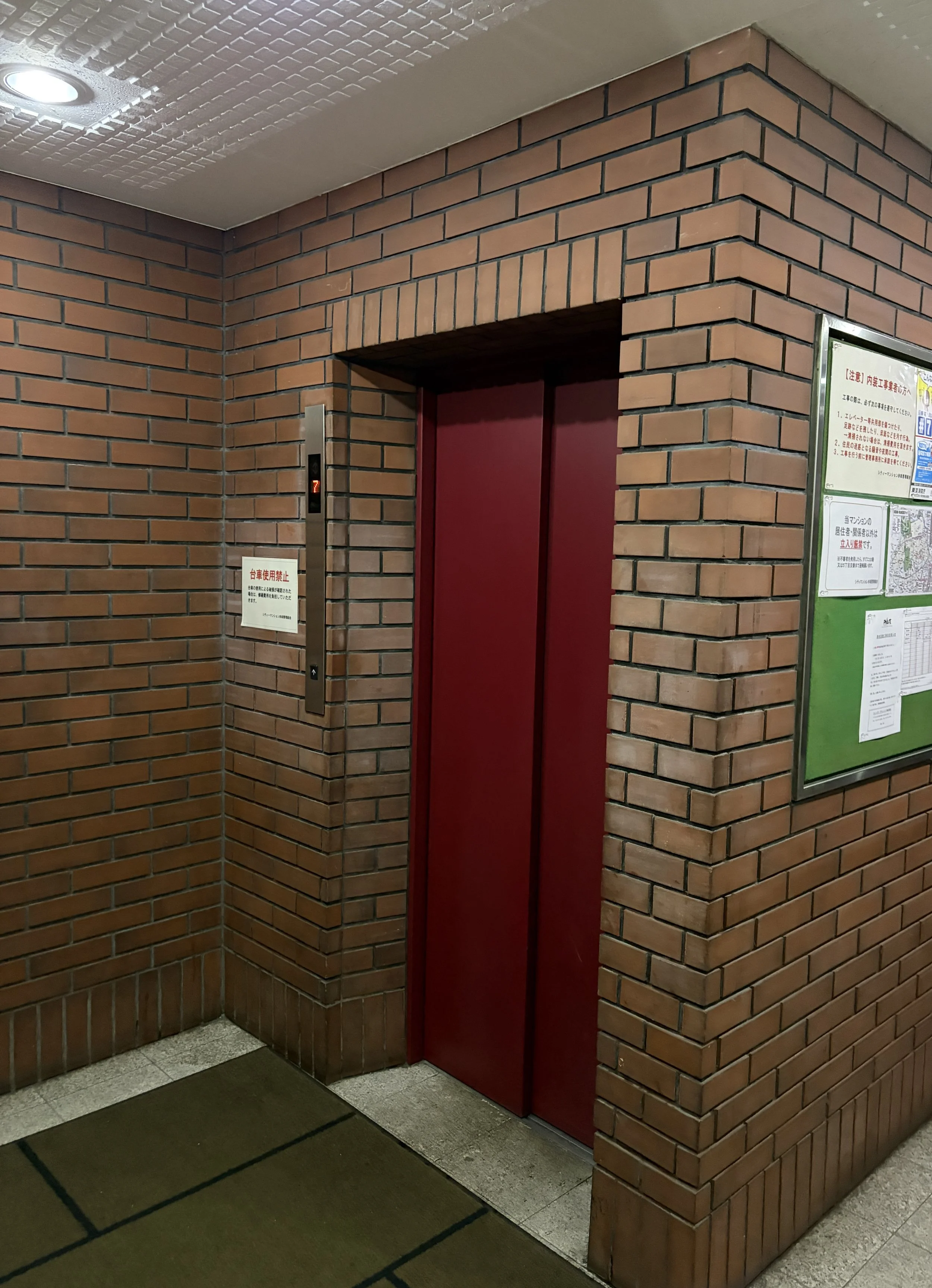 赤いエレベーターの扉が閉まっている、レンガ造りの壁と案内表示板がある公共スペースの写真