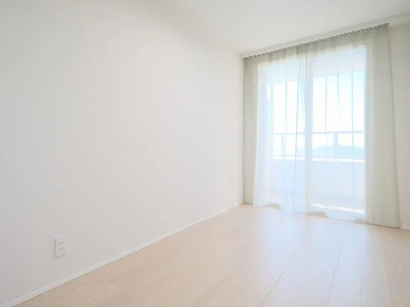 白い壁と木製の床、窓とカーテンがある空き部屋