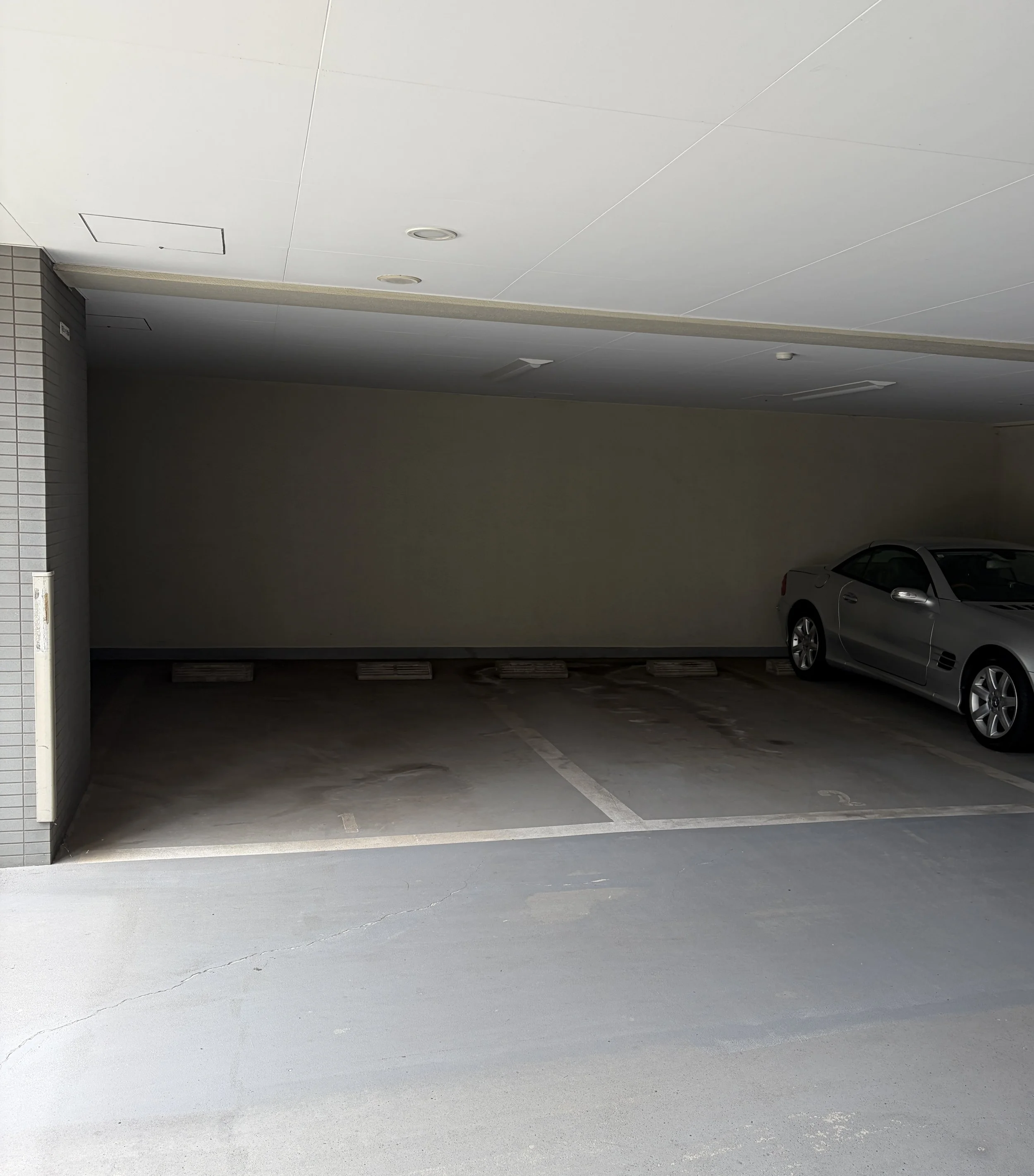 駐車場の空きスペースと停まっている車。建物の一部と駐車スペースのラインが見える。
