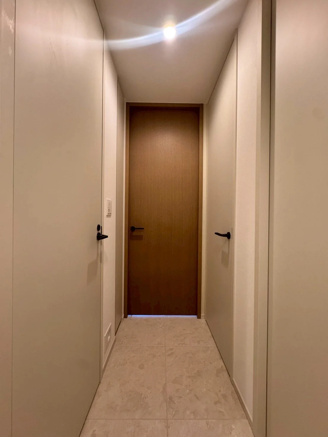 廊下の奥に木製の扉があり、左右に白い扉がある indoor hallway with wooden door at the end and white doors on both sides.