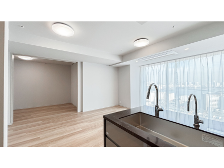 明るいリビングルームとキッチンエリア、白い壁と木製フローリング、窓に白いカーテン.