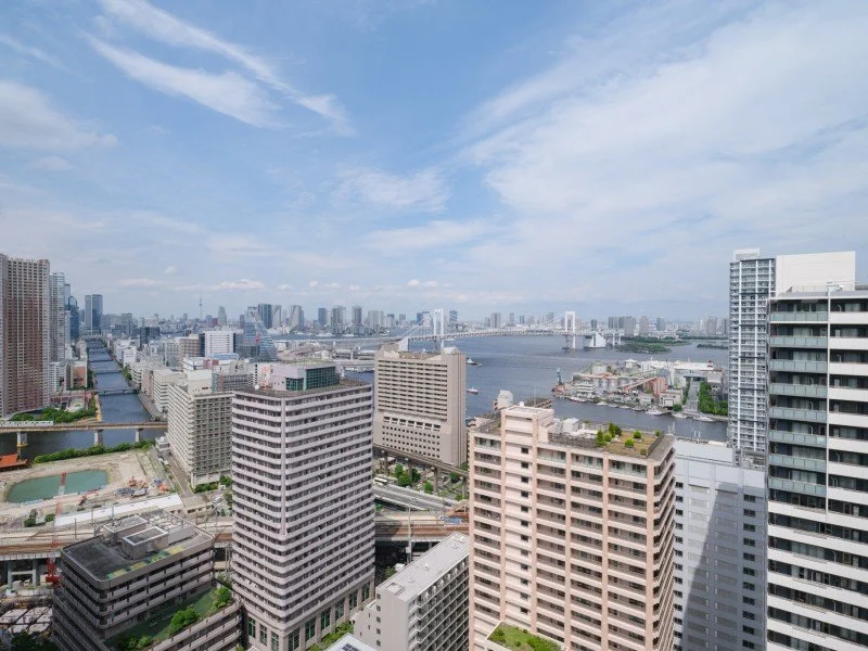 都市の高層ビル群と川が見える市街地の景色、青空と雲が広がっている