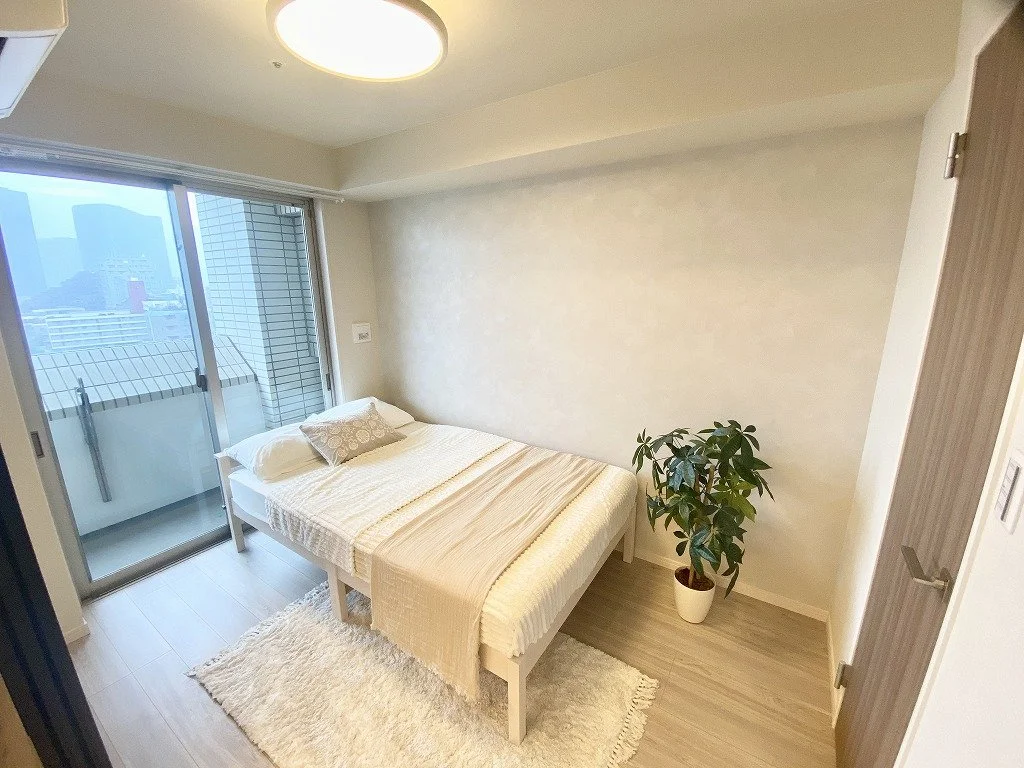 シンプルでモダンな寝室、白いベッド、観葉植物、バルコニーの窓から都市の景色が見える