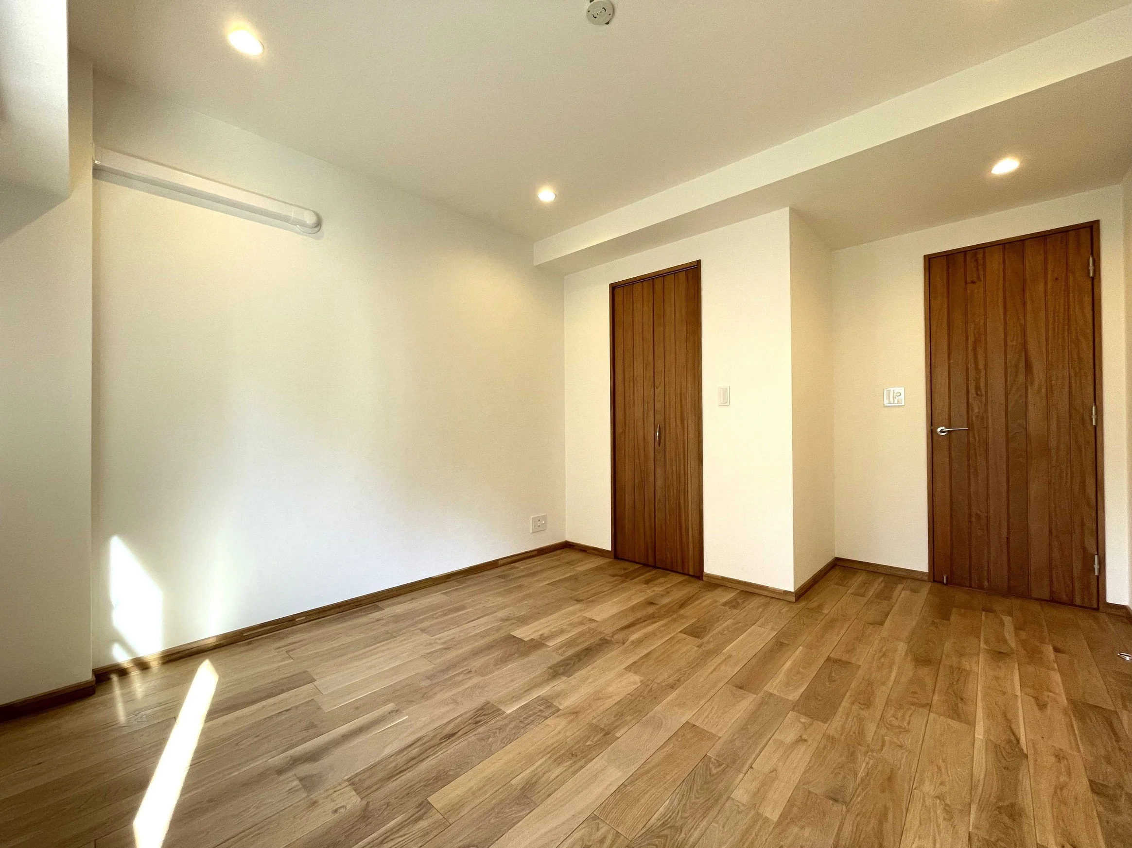 木の床と白い壁の部屋、木製の扉が2つあり、天井にLEDライトと火災報知器が設置されている