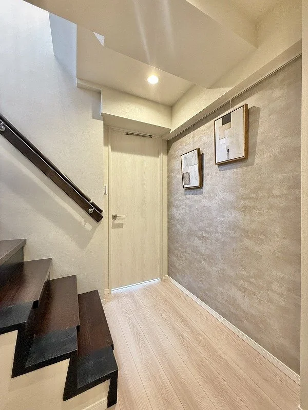 階段の下に扉がある玄関ホール。壁に2枚の抽象画が掛かっている。