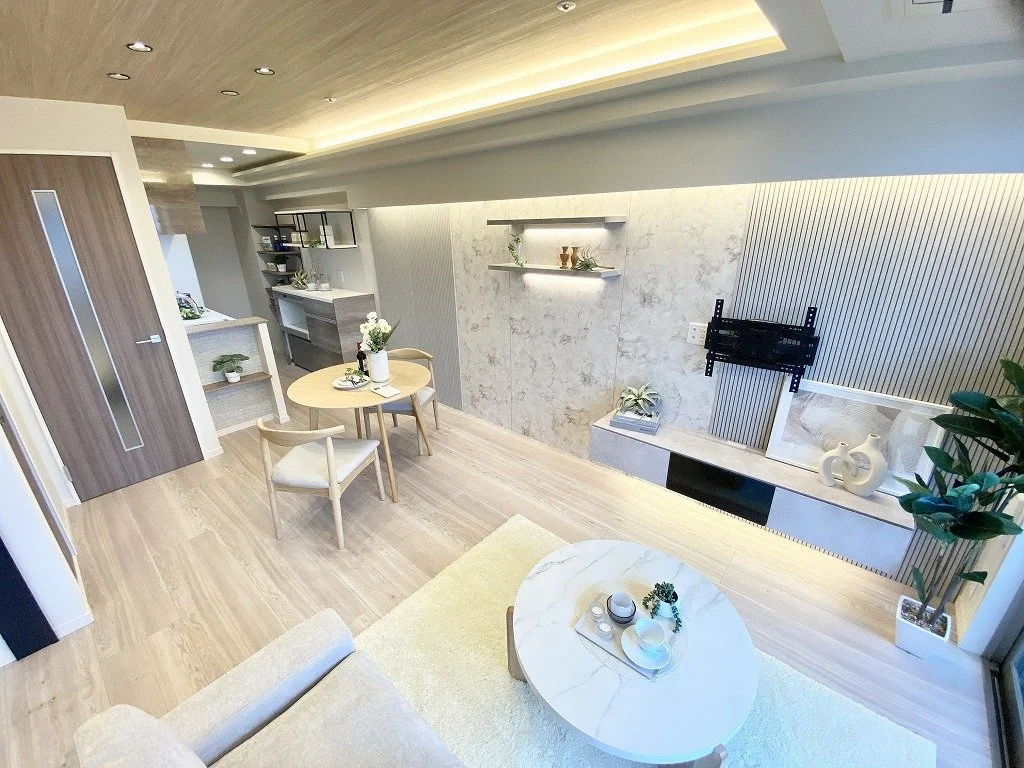 シンプルでモダンなリビングルームとダイニングエリアの内観。木製の床と天井、壁には棚や装飾品が配置されている。テレビの取り付け位置も見える。