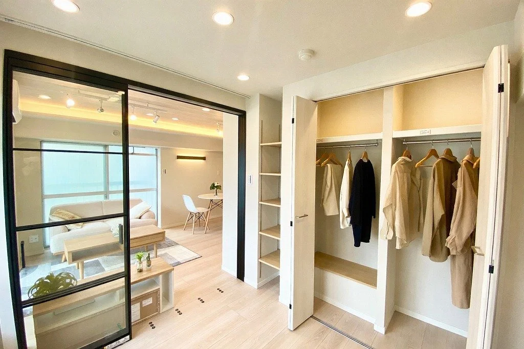 リビングルームとクローゼットのある部屋の写真。クローゼットには洋服が掛かっている。