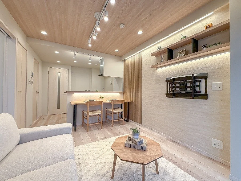 木製の天井と床のリビング、キッチンのカウンターに2脚の椅子、壁に棚とテレビ台、ソファとコーヒーテーブルがある部屋の interieur