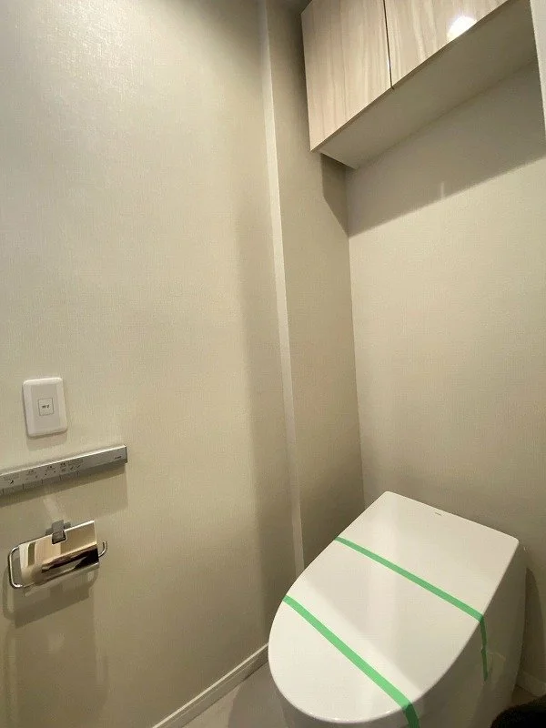 トイレと棚、壁のコンセントとペーパーホルダーがあるトイレのイメージ