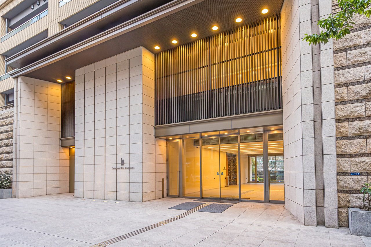 現代的な建物のエントランス。ガラス扉と石造りの外壁、照明が点灯している。