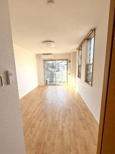 空のリビングルーム、木製フロア、大きな窓とバルコニーのドア、白い壁とカーテン