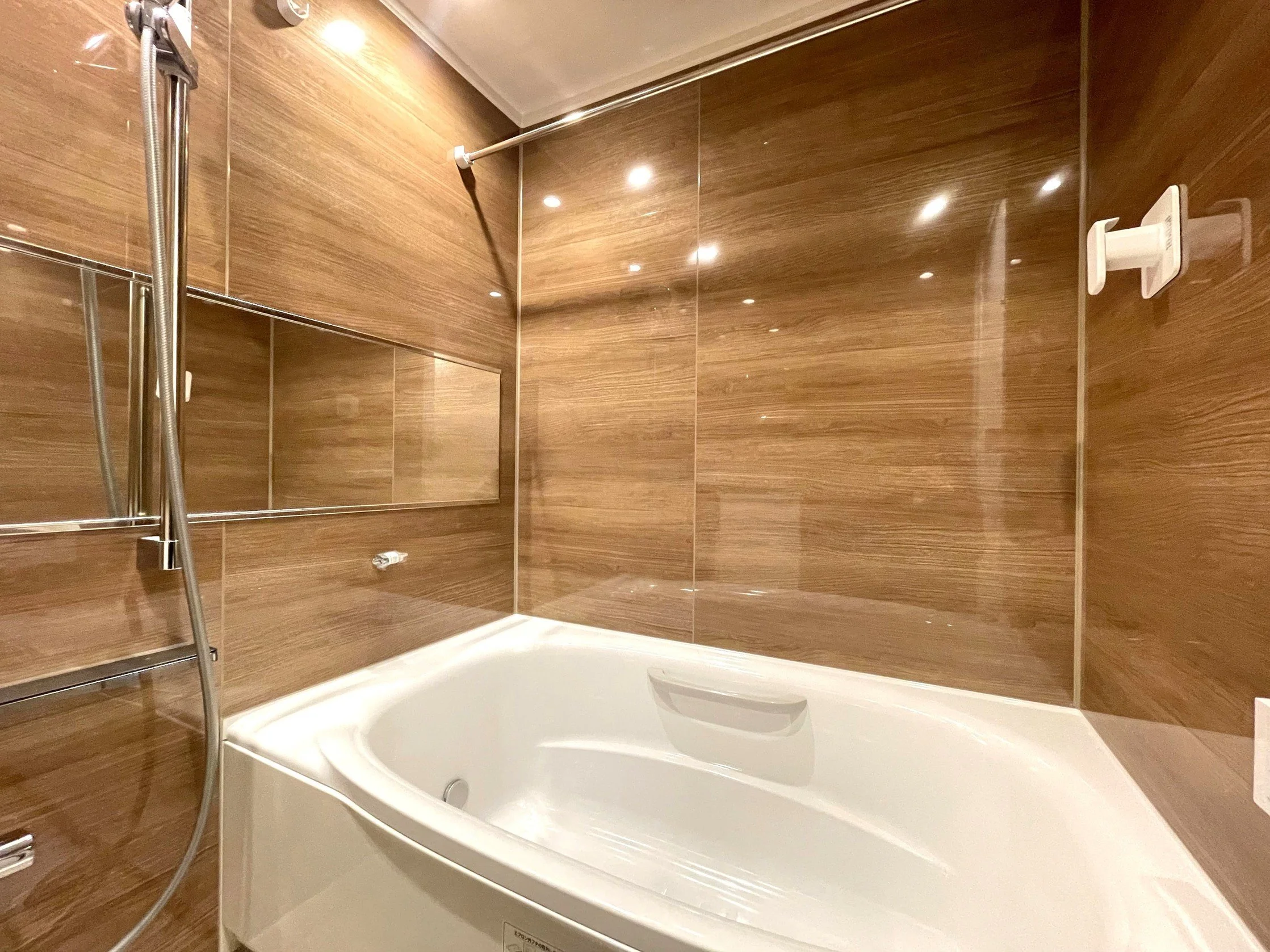 木目調の壁と浴槽がある浴室の様子。シャワーとミラーも設置されている。