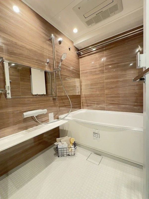 木目調の壁に鏡とシャワー、浴槽とバス用品のバスケットがあるモダンな浴室