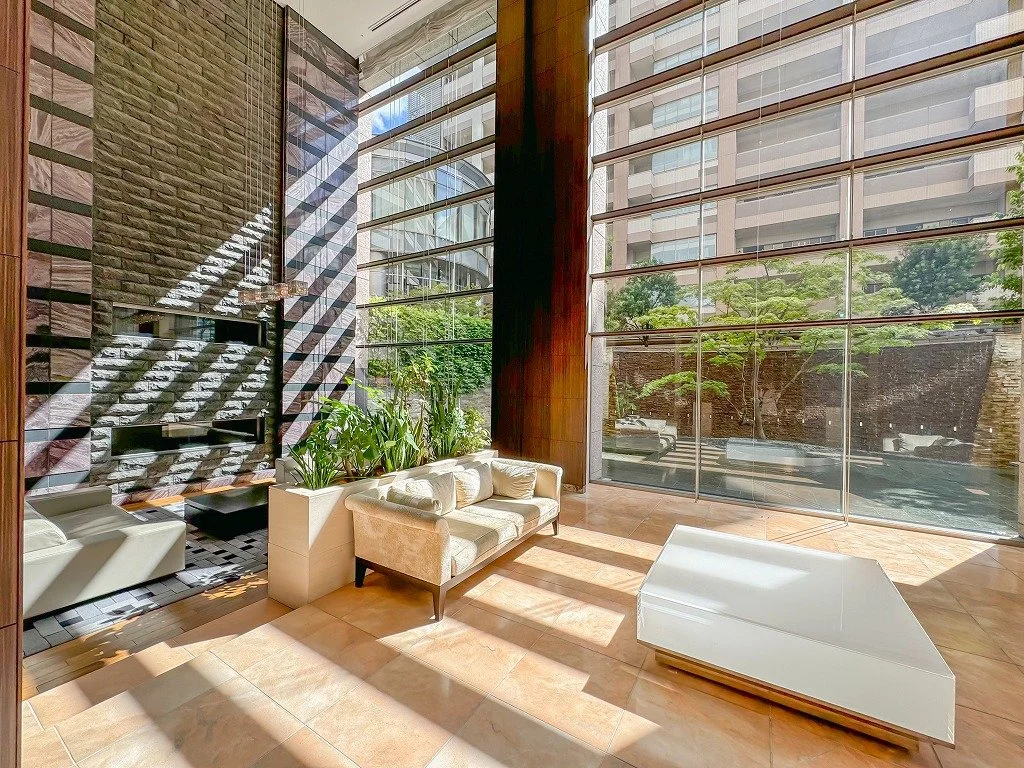 自然光が差し込む高級なロビー、白いソファと緑の植物、公園に面した大きなガラス窓