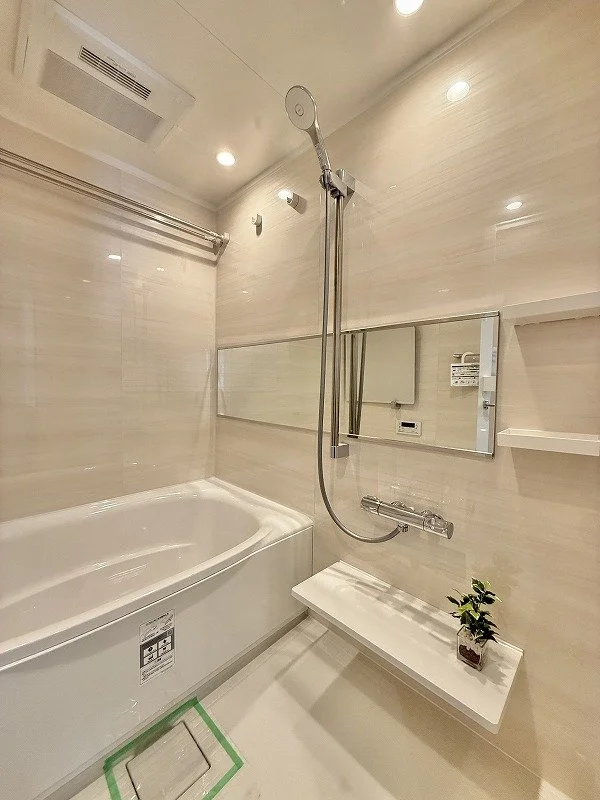 シンプルでモダンな浴室、白いバスタブと壁掛けシャワー、鏡と棚、小さな観葉植物が置かれている。