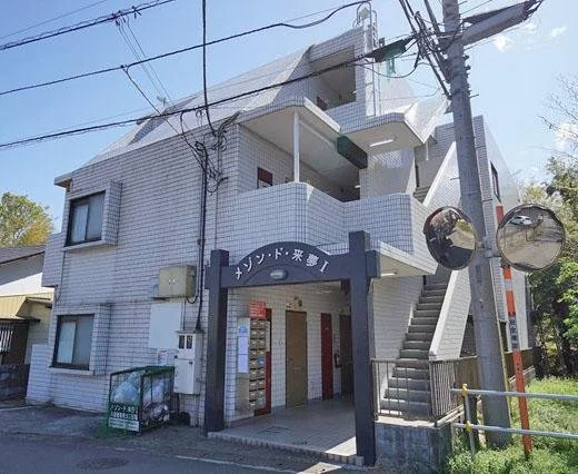 白いタイルの三階建て建物、入り口に黒いアーチと看板、階段とバルコニー、電線と電柱、左右に鏡のついた標識