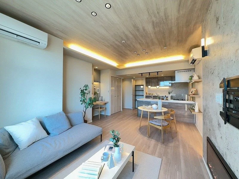 モダンなリビングとダイニング、キッチンが一体になった広々とした空間。木材の天井と床、白を基調としたインテリアが落ち着いた雰囲気を醸し出している。ソファ、ダイニングテーブル、テレビ、観葉植物などが配置されている。