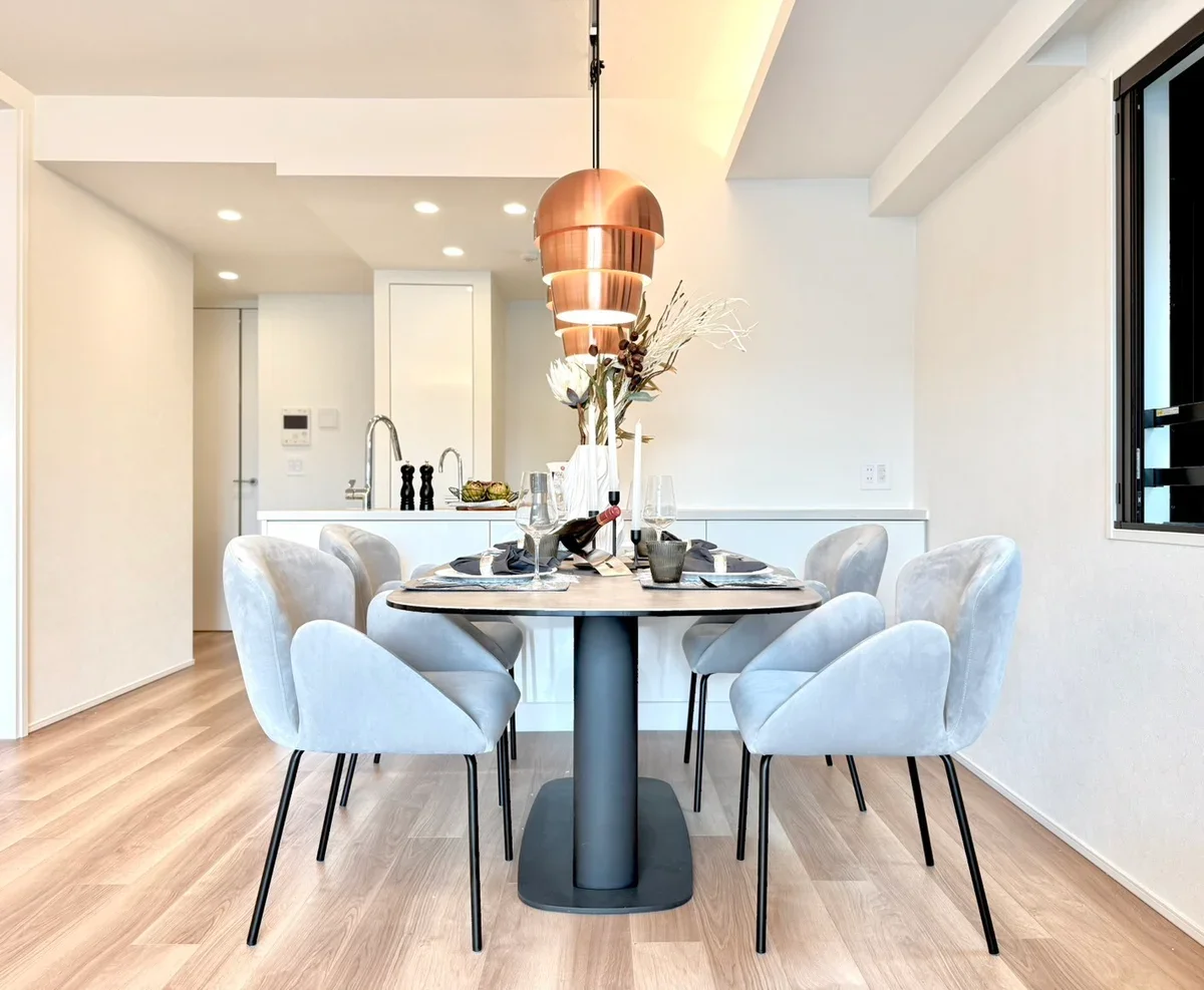 白い椅子とダイニングテーブル、花瓶に花や枝を飾り、酒瓶とグラスが置かれているダイニングルームの写真