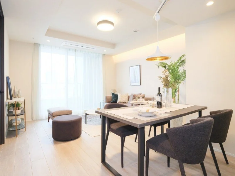 明るいリビングルームとダイニングエリア。ソファ、椅子、植物、テーブル、装飾が配置されたシンプルでモダンなインテリア。