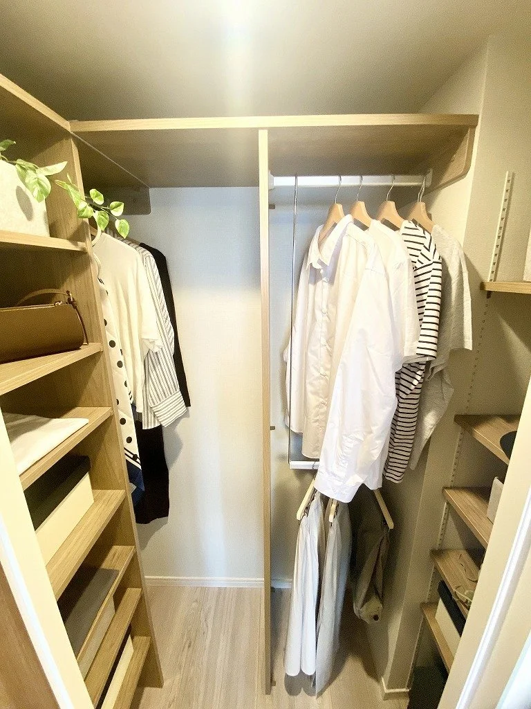 クローゼットの中に白やストライプのシャツや衣料品が掛けられ、棚に物が収納されている様子。