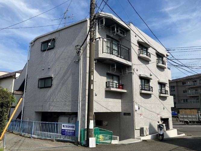 三階建ての白いアパートメントの建物。バルコニーと窓があり、電線が通っている。
