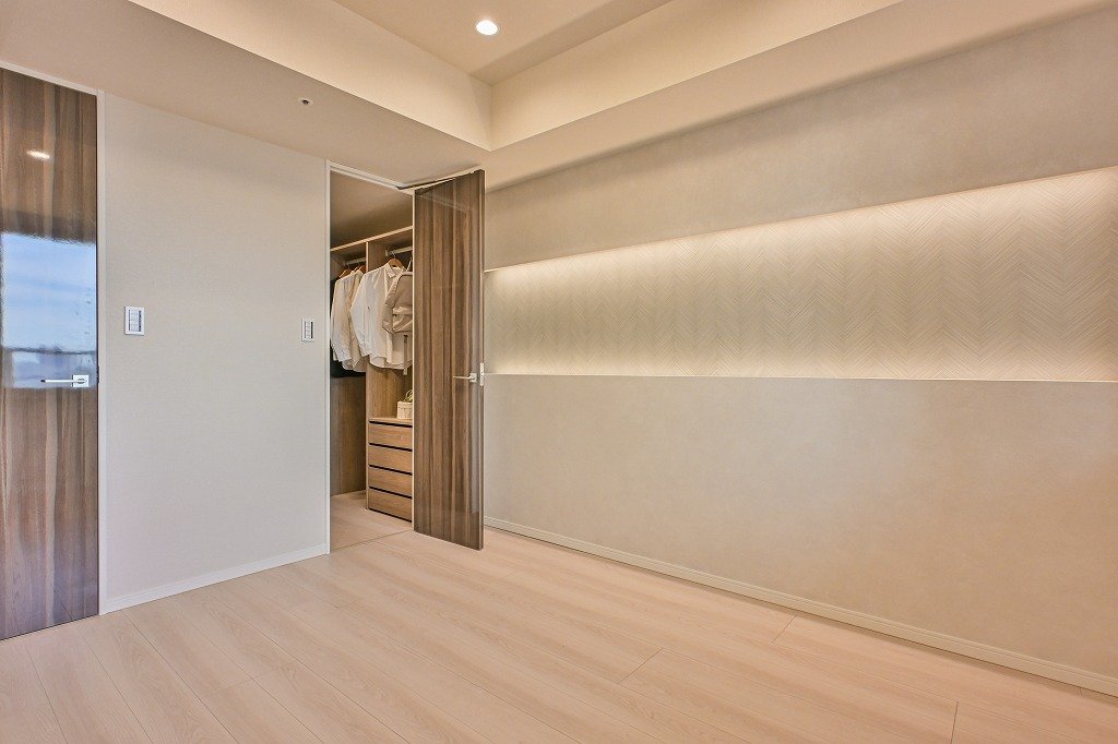 洋室の一角にクローゼットがあり、ドアが少し開いている。クローゼット内には白いシャツやブラウス、収納用の引き出しが見える。