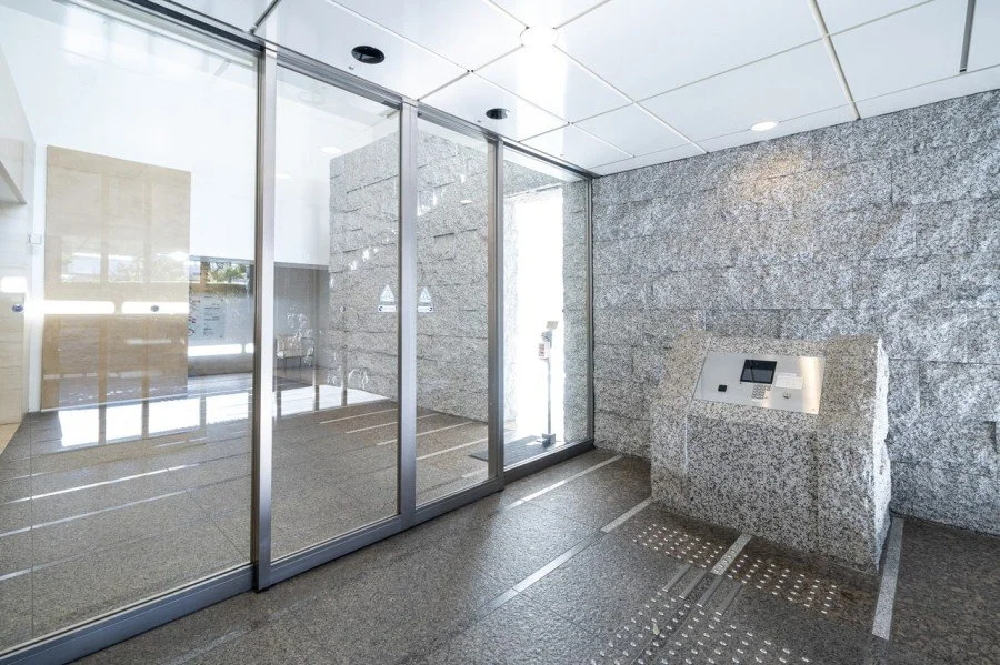 ガラスの扉と石の壁のエントランスホール、自動受付機、清潔な床面。