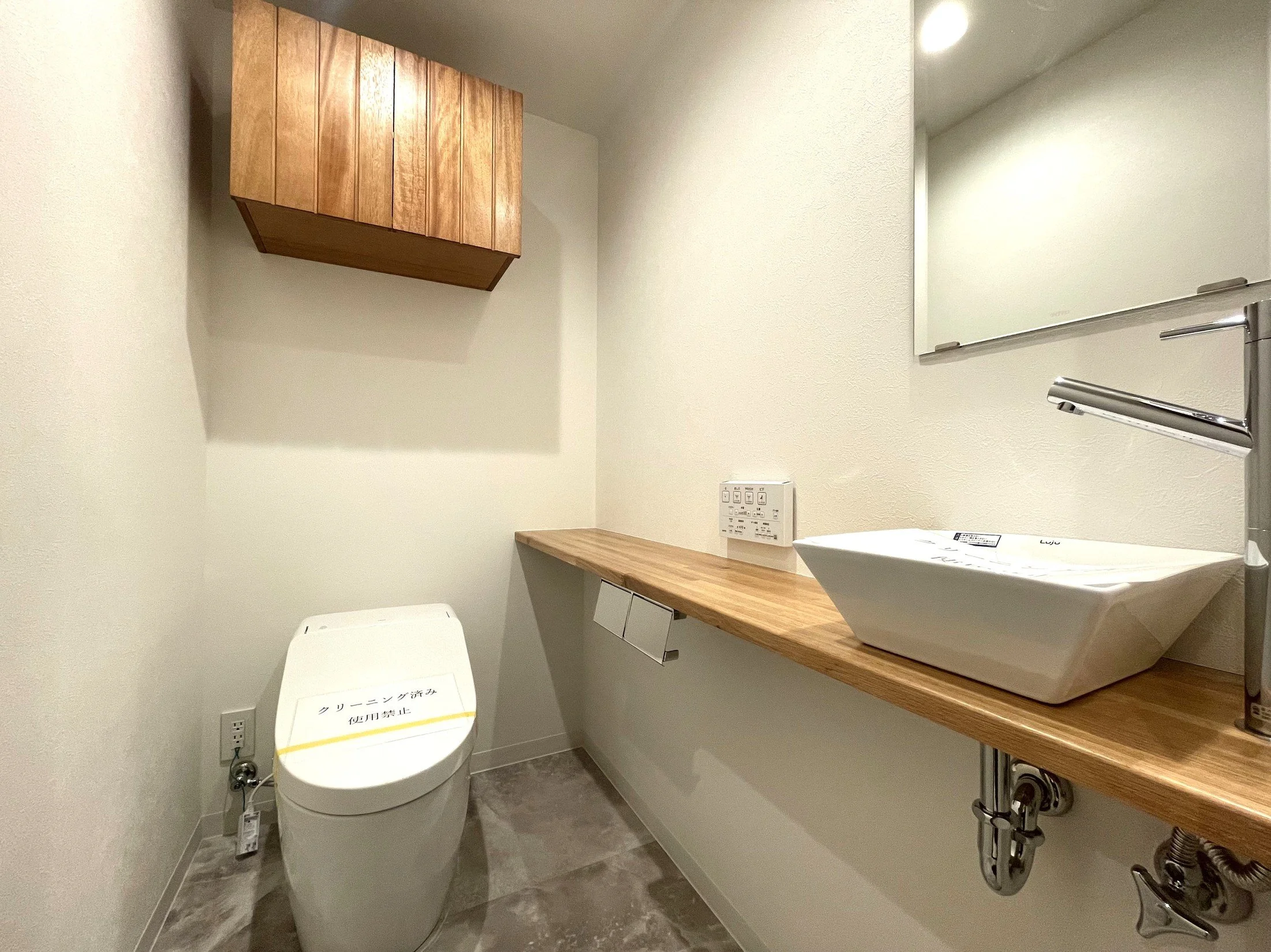 白い壁と木製の棚、鏡とシンクのあるトイレの内装。