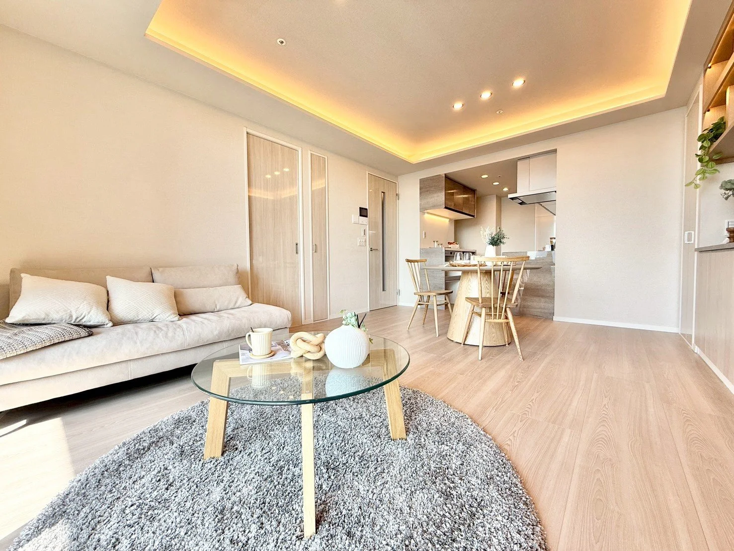 ナチュラルでモダンなリビングルームとダイニングエリア、木製の家具と白い壁、ソファと丸いガラステーブル、暖色照明が印象的な interior