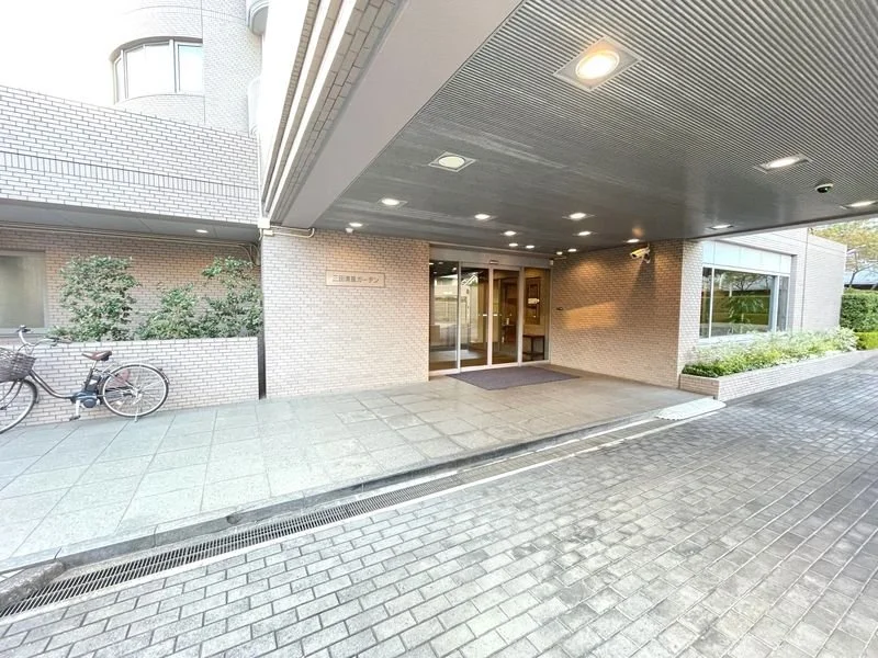 ビルのエントランス入口と自転車と植え込みが見える。