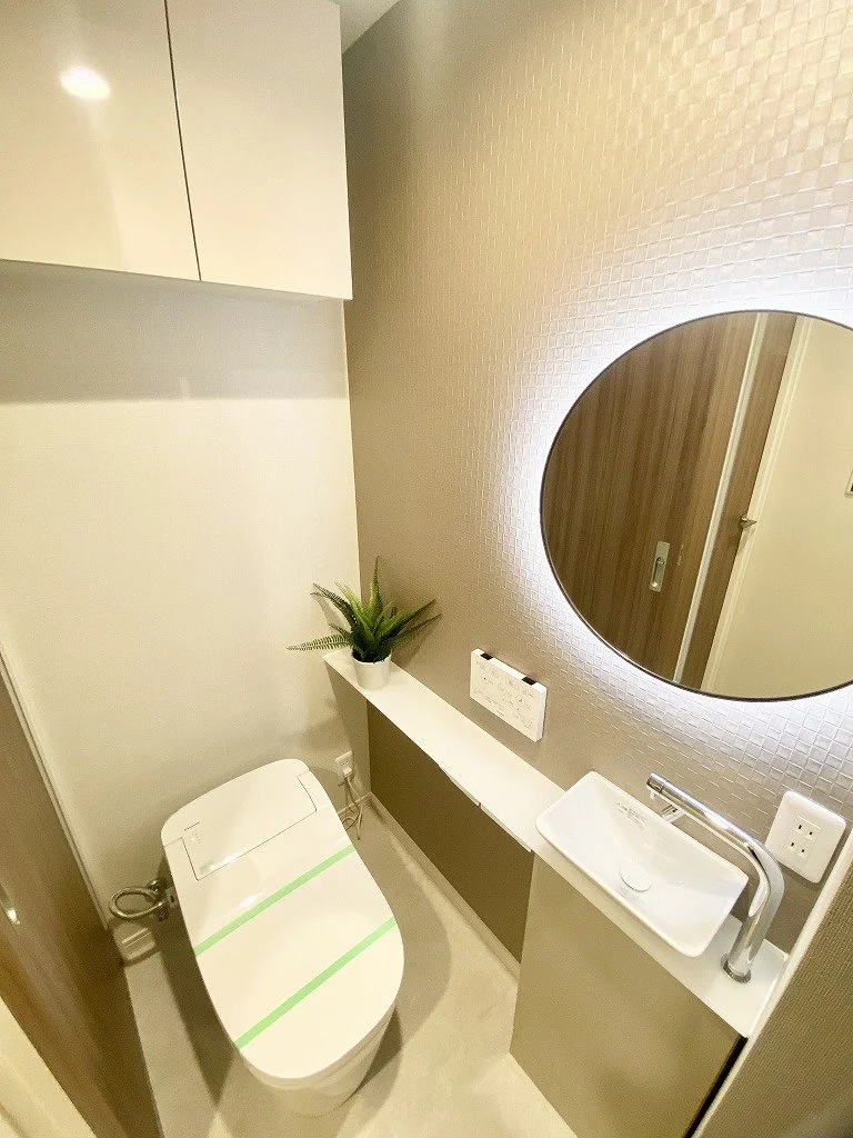 コンパクトな洗面台と便座付きトイレ、壁に丸い鏡と植物が置かれたシンプルなバスルームの interior.