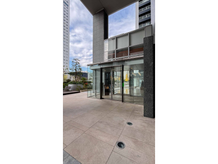 高層ビルの外にある建物の入り口、ガラスの扉と階段が見える。