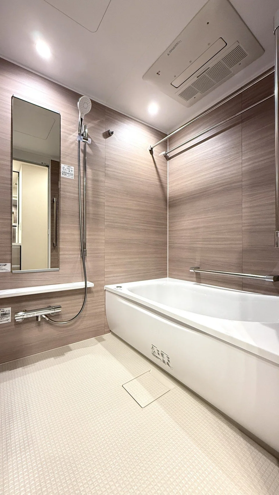 木目調の壁の浴室で、白い浴槽とシャワーが付いている。鏡と棚、手すりも設置されている。