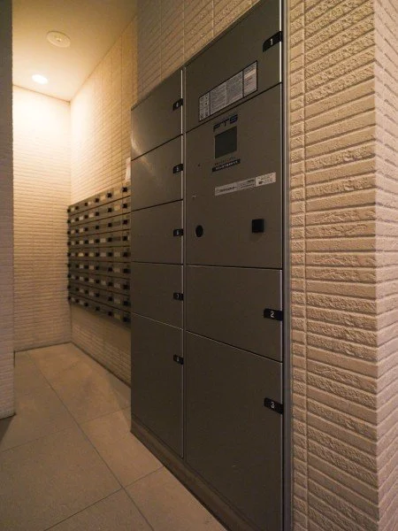建物の郵便受けと宅配ボックスが設置された共用スペースの壁面。邮筒と荷物受けが並んでいる。