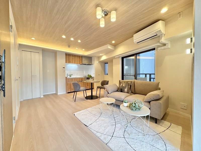 リビングルームとキッチンがある現代的な居住空間。ソファとコーヒーテーブル、ダイニングセット、家具や照明が配置されている。大きな窓から自然光が入る。