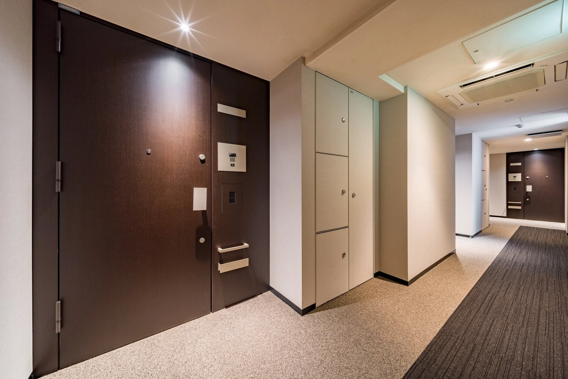 ホテルのエントランス廊下、ダークブラウンのドアと金庫付きのロッカー、照明とカーペットの床。