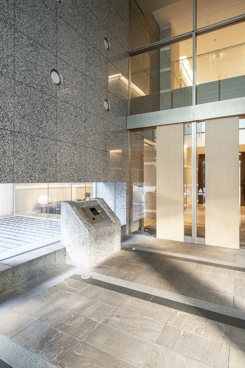 モダンな建物のエントランス、ガラスの扉と石の壁、インターホンのパネルが設置されたコンクリートの台。